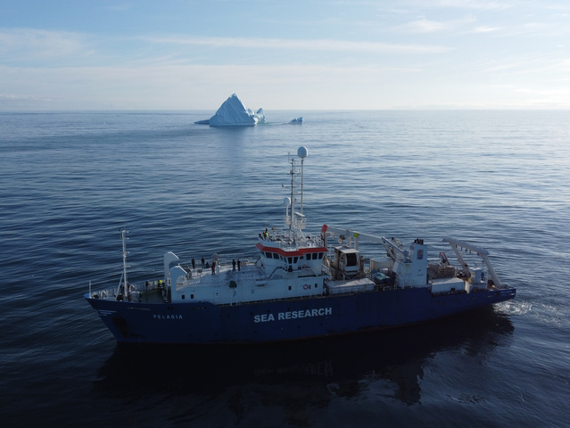 The image shows the RV Pelagia from NIOZ (Royal Netherlands Institute for Sea Research) in the foreground, with an iceberg in the background in the open North Atlantic.
